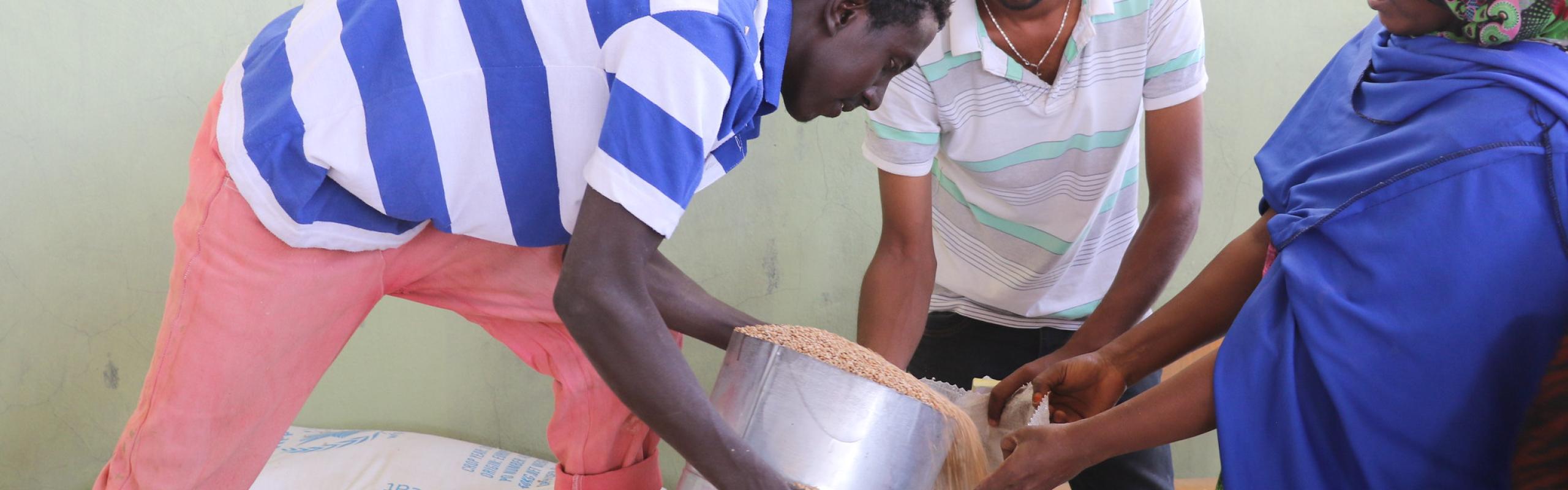 Two men pour grain into a bag held by a woman in a refugee camp in Ethiopia