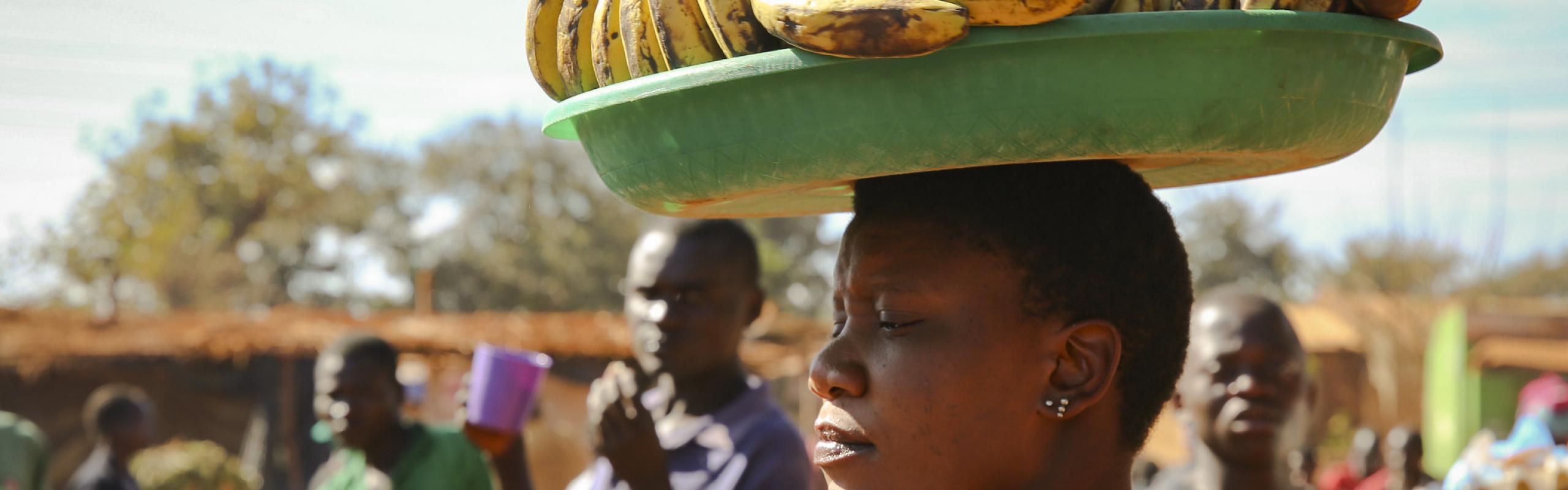 Une femme porte un plateau de fruits sur la tête dans un marché de village au Malawi