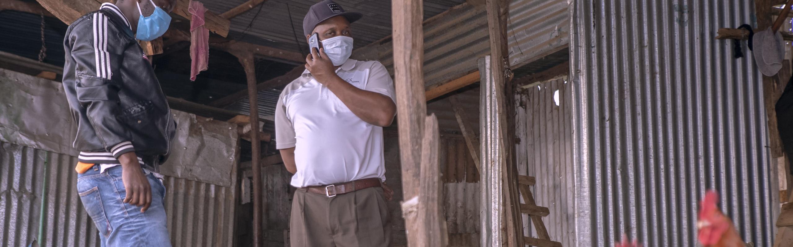 Two male Male poultry farmers wearing medical face masks stand with their flock in Kenya