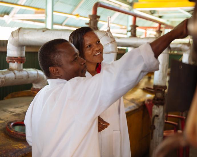 Smiling Factory Manager at Mount Meru Sunflower Seed Oil Processing Factory inspecting factory equipment with worker - Arusha, Tanzania