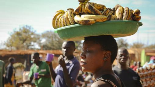Une femme porte un plateau de fruits sur la tête dans un marché de village au Malawi