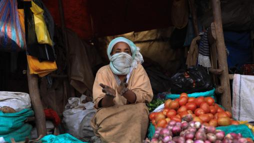 ne femme portant un masque facial en tissu est assise sur le marché de Saris en Éthiopie, entourée de sacs en tissu et de tas d'oignons, de pommes de terre et de tomates.