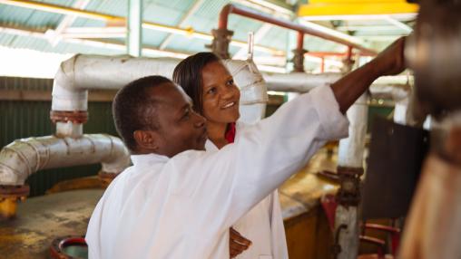 Smiling Factory Manager at Mount Meru Sunflower Seed Oil Processing Factory inspecting factory equipment with worker - Arusha, Tanzania